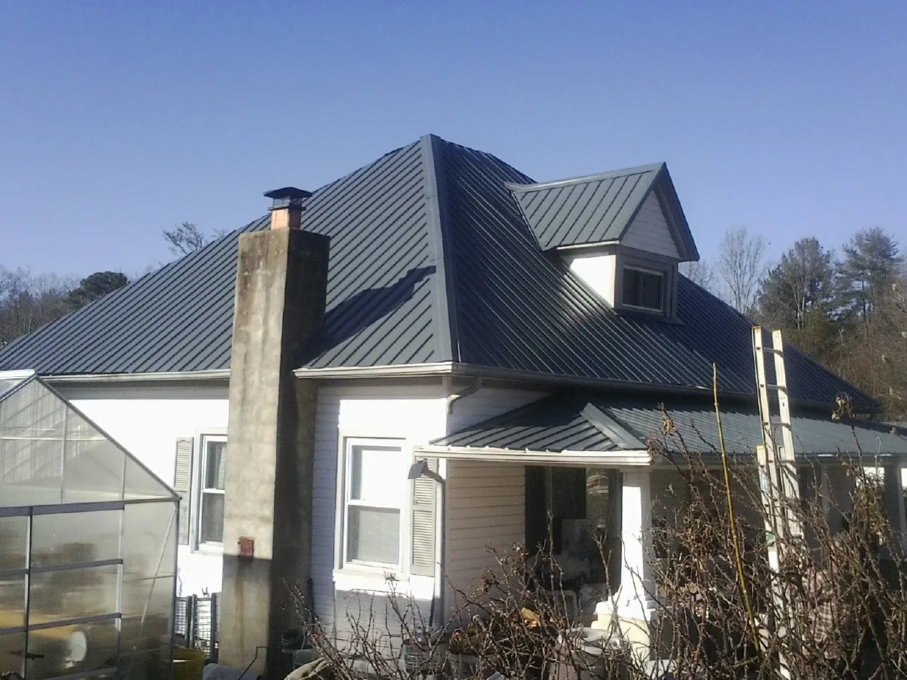 Dark blue standing seam metal roof on a white farmhouse with dormer — Slate & Tile Roof Repair by Roofing Brothers in League City