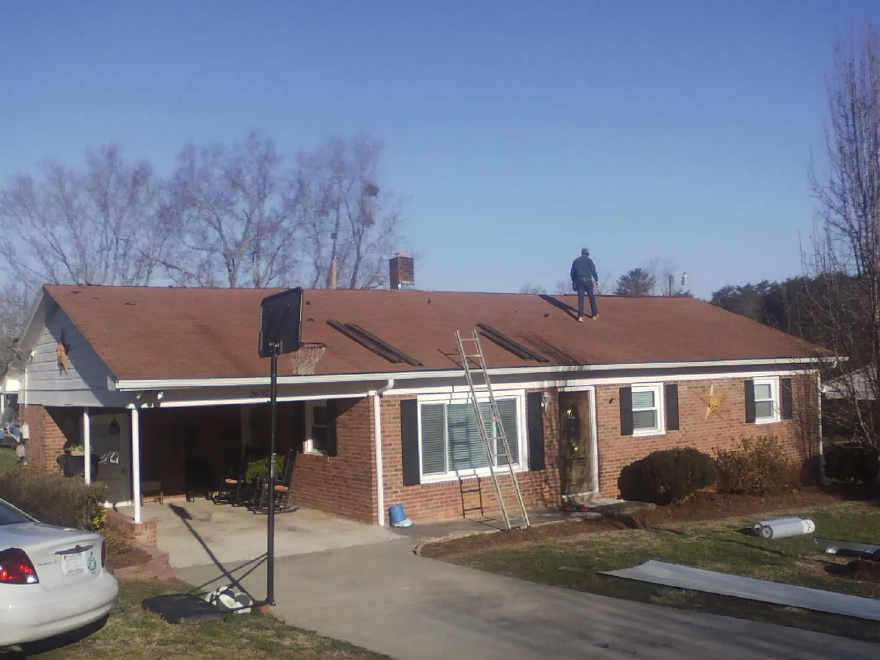 Roofer stripping a shingle roof on a brick ranch before metal panels in League City