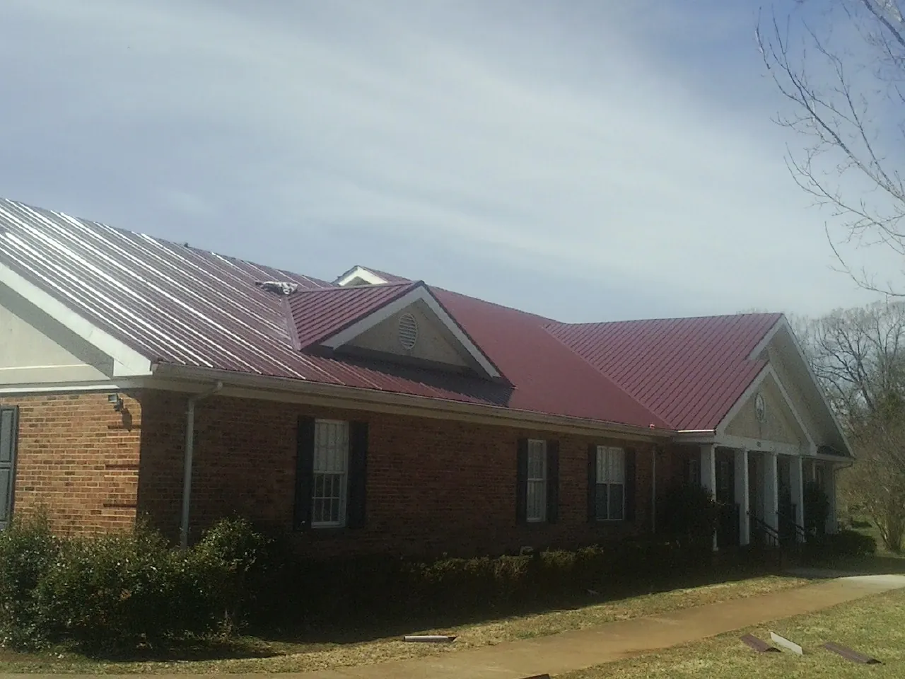 Red metal roof with gabled entries on a long brick building, from a Hail Damage Roof Repair job in League City