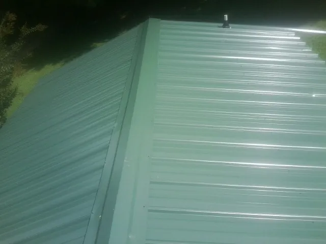 New green metal panels meeting at the ridge of a roof — Flat Roof Repair work by our crew in League City
