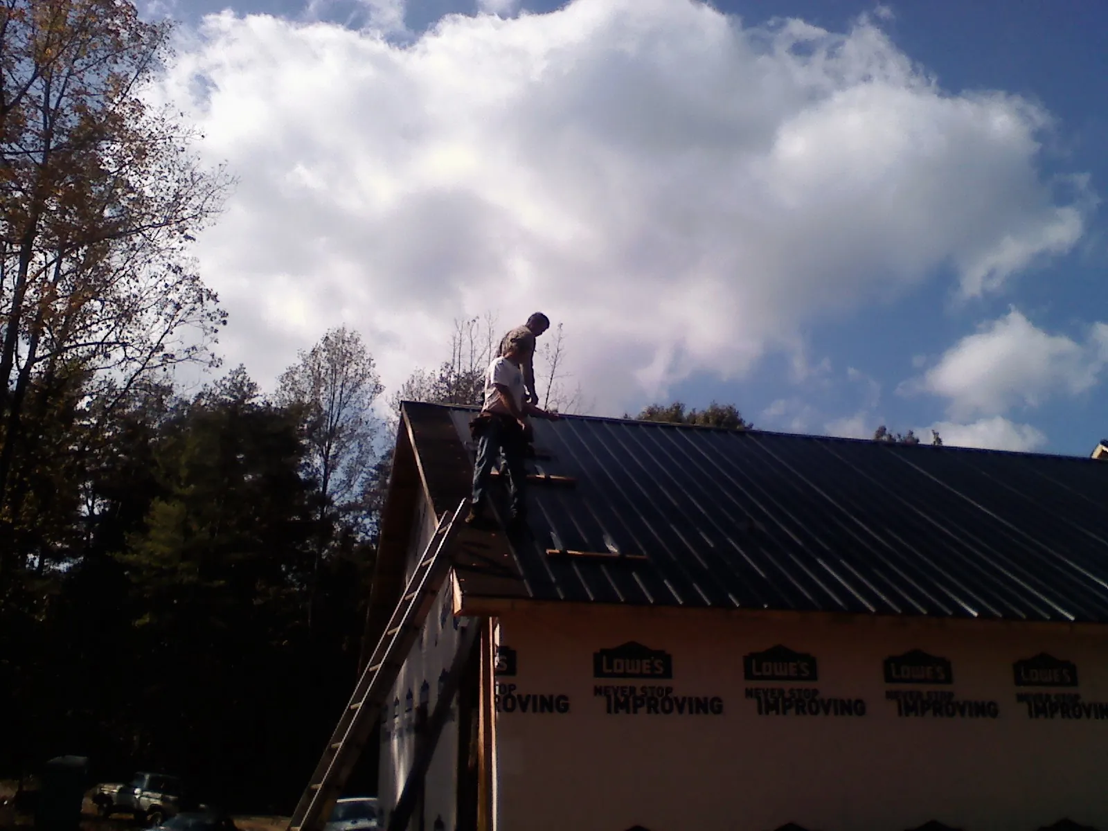 Roofer fastening dark metal panels high against a cloudy sky, from a Roof Inspection job in League City