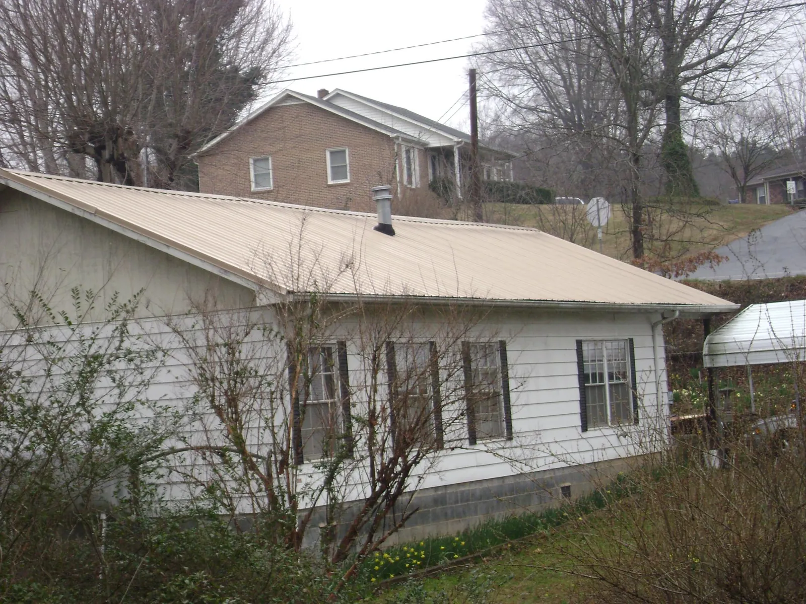 Tan metal roof on a white sided house set into a hillside — Commercial Roofing by Roofing Brothers in League City